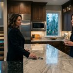 A composed woman faces her husband and longtime best friend during a tense early-morning confrontation inside her upscale kitchen.