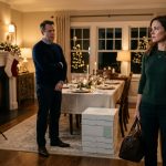 Woman holding an overnight bag after her husband excluded her from Christmas as a suspicious holiday photo setup waits behind them