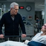A 67-year-old father standing beside his daughter in the ICU after discovering her serious injuries.