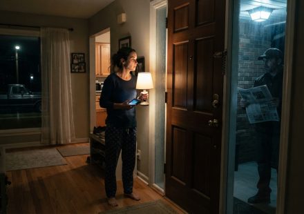 A woman watches a stranger holding a newspaper outside her home after her parents publicly called her a failure and exposed her private information.