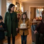 Mother stands protectively beside her two children after they arrive at their grandfather's decorated home for Christmas.