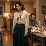 A woman in a cream blouse and green skirt stares at her niece holding an empty glass after her sister's daughter tossed her drink during a birthday dinner.