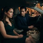 Hannah looks concerned inside a parked car as her husband protects her canvas tote outside Grandma's 85th birthday celebration.