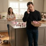 Father holding tiny pink birthday crowns while receiving a disappointing phone call as his one-year-old daughter plays on the kitchen floor.