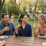 A woman calmly raises her drink after her sister mocks her during a crowded summer family picnic.