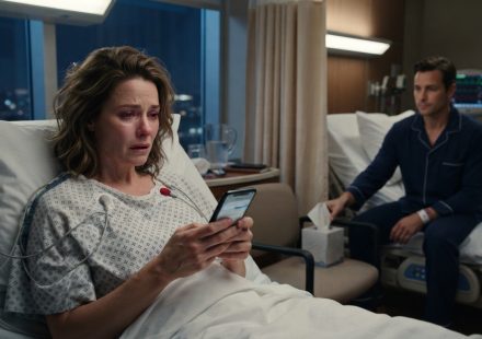 A woman in a hospital bed reading a troubling message on her phone while a male patient watches quietly from the neighboring bed.