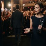 Madison holding her award and a mysterious brass key after leaving the stage while a man in a charcoal suit disappears into the crowd.