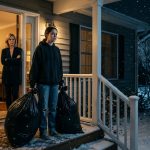 A teenage girl holding two black garbage bags outside her family home on a snowy night while her stepmother stands in the doorway and her father remains inside.