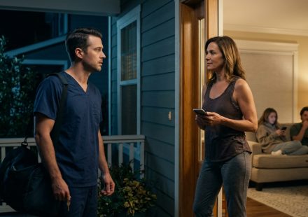 An exhausted male doctor in medical scrubs holds his house key while his stepmother blocks the doorway of their family home at night.
