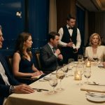 A composed father sits beside his uncomfortable daughter at an elegant restaurant table while her wealthy future in-laws speak dismissively to a waiter.