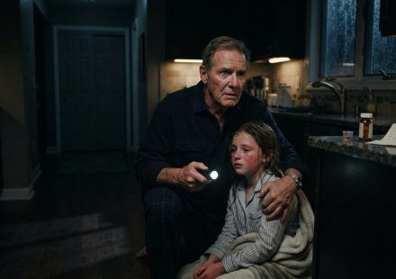 A worried retired grandfather answering his granddaughter’s emergency phone call late at night while rain falls outside.