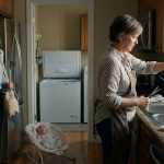 Shocked mother standing in her kitchen as her mother-in-law pours stored breast milk down the sink beside a pile of empty storage bags.