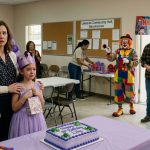 A heartbroken eight-year-old girl in a lavender dress watches her uncle and a clown take over her birthday celebration at a community hall.