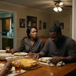 A shocked wife sits at a family dinner table as her younger sister announces her pregnancy and points toward the woman's silent husband.