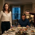 Angry mother-in-law pointing toward the door during New Year's dinner while her daughter-in-law holds her coat and her husband looks away.