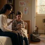 A concerned mother comforts her nine-year-old daughter on a bedroom bed after the child comes home crying from school following a teacher's cruel remark.
