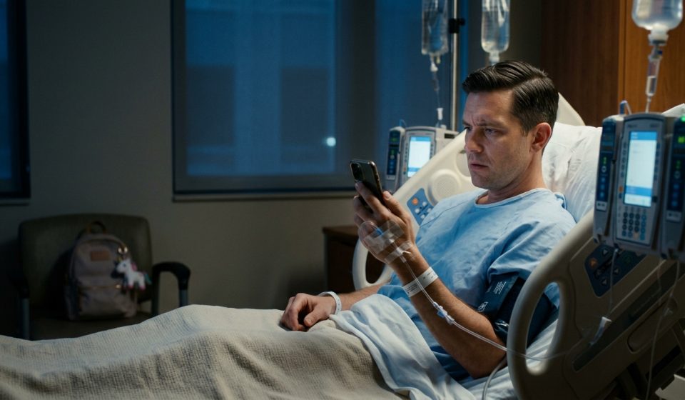 A man recovering from emergency appendix surgery lies in a hospital bed, holding a phone as his mother asks him to babysit his sister's children.