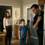 A concerned mother and her eight-year-old son watch as a police officer examines a fishing-trip photograph attached to their kitchen refrigerator.