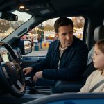 A concerned father looks toward his frightened seven-year-old daughter inside a parked pickup truck, with a school carnival glowing in the background.