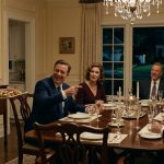 An eighteen-year-old woman holding a tray of appetizers while her parents and their guests laugh at her during an elegant family dinner party.