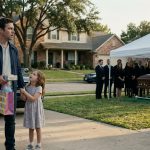 A shocked father holding gifts stands beside his frightened six-year-old daughter outside their family home, where a funeral for his wife is taking place.