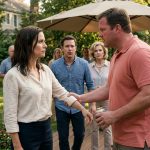 An athletic woman with beer-soaked hair and a wet blouse stands on a backyard patio while her angry brother-in-law grips her wrist during a family barbecue.