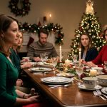 A shocked young woman in a green dress standing beside a Christmas dinner table while her mother in a red sweater criticizes her in front of the family.