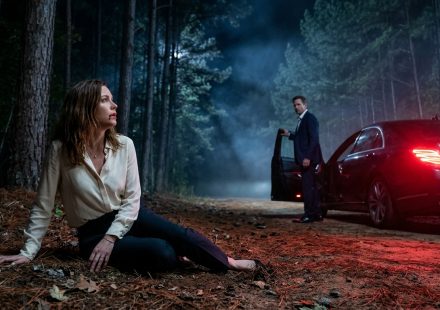 A frightened woman sits beside a secluded forest road at night while her husband stands near a luxury sedan after abandoning her during a medical emergency.