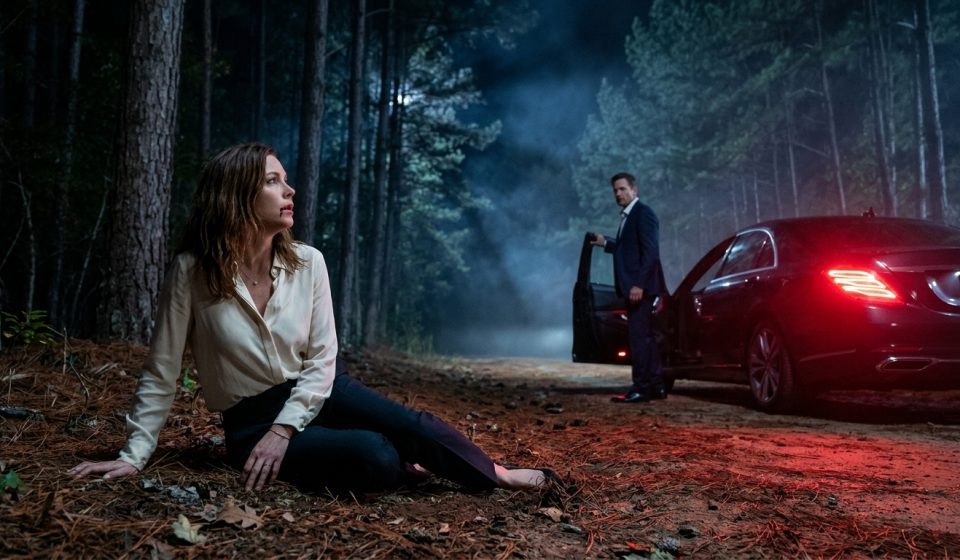 A frightened woman sits beside a secluded forest road at night while her husband stands near a luxury sedan after abandoning her during a medical emergency.