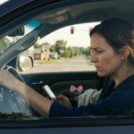 A worried mother sits inside her SUV at a red traffic light, holding herself together while looking at a mysterious message on her phone after learning her young daughter has been injured.