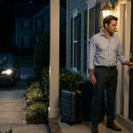 A shocked businessman stands outside his suburban home at night with two suitcases, trying his key in a newly changed door lock beside a handwritten note.