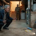 A retired pediatric emergency professional cautiously approaches a frightened young boy hiding beside a water heater in a residential basement.