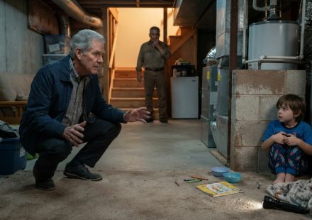 A retired pediatric emergency professional cautiously approaches a frightened young boy hiding beside a water heater in a residential basement.