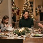 Mother making a serious Christmas announcement while her daughter and young grandchildren sit around the family dinner table.