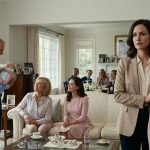 A twelve-year-old girl in a navy-blue dress struggles to smile while her grandparents celebrate her baby cousin in an elegant family living room.
