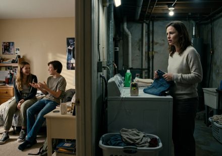 A stepmother stands beside a clothes dryer holding jeans, shocked by a conversation coming through a forgotten baby monitor in her basement laundry room.