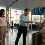 A shocked wife watches her husband hand her first-class boarding pass to his smiling mother at an airport terminal before their anniversary trip to Hawaii.
