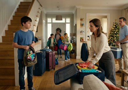 A disappointed 13-year-old boy holding his packed backpack watches his parents prepare for a Christmas family vacation while his three siblings get ready to leave without him.